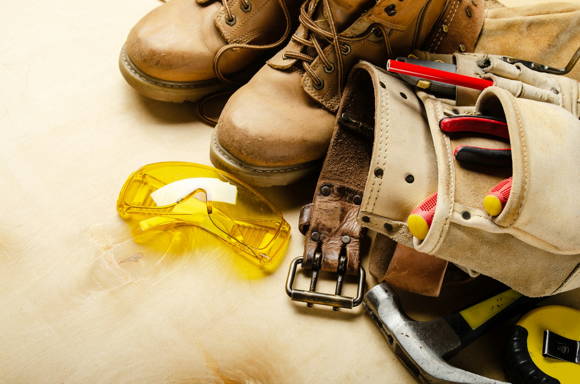 Construction concept background of toolbelt yellow boots goggles ant tools on plywood